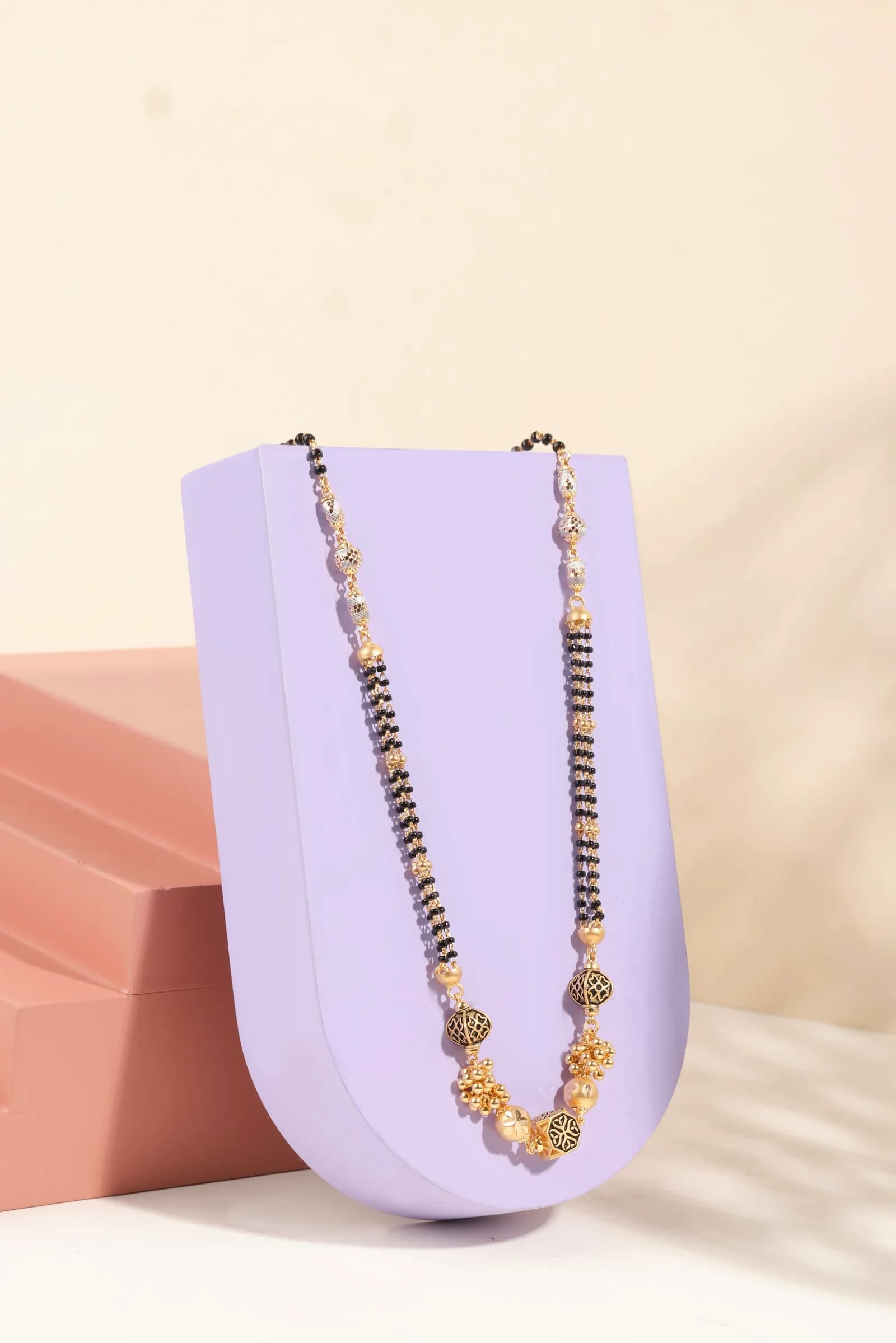 Tanmaniya 22K Gold Mangalsutra - A gold and black beaded mangalsutra necklace draped over a purple display stand